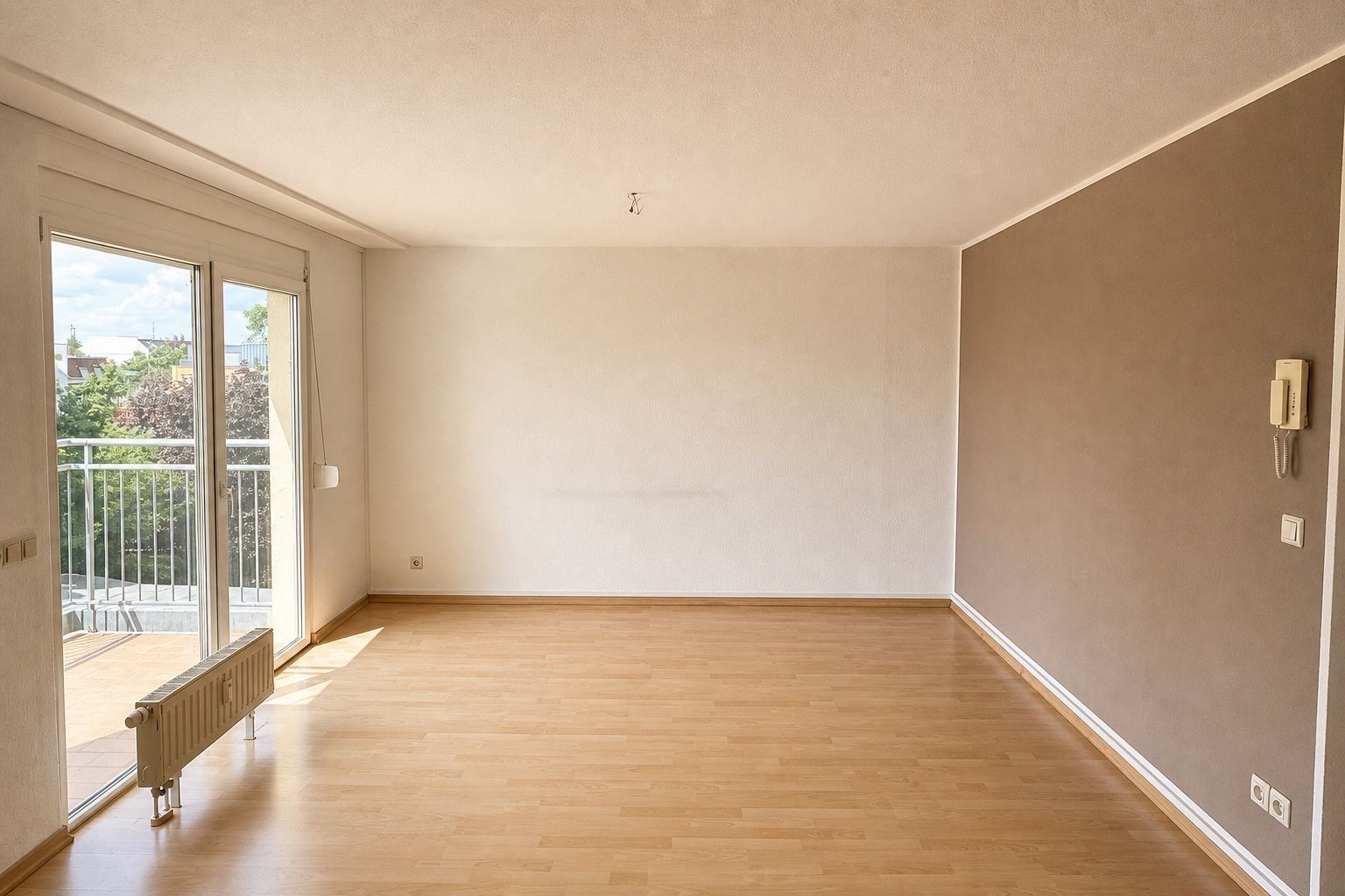 Großes, leeres Zimmer mit heller Fensterfront, Balkonzugang und brauner Akzentwand