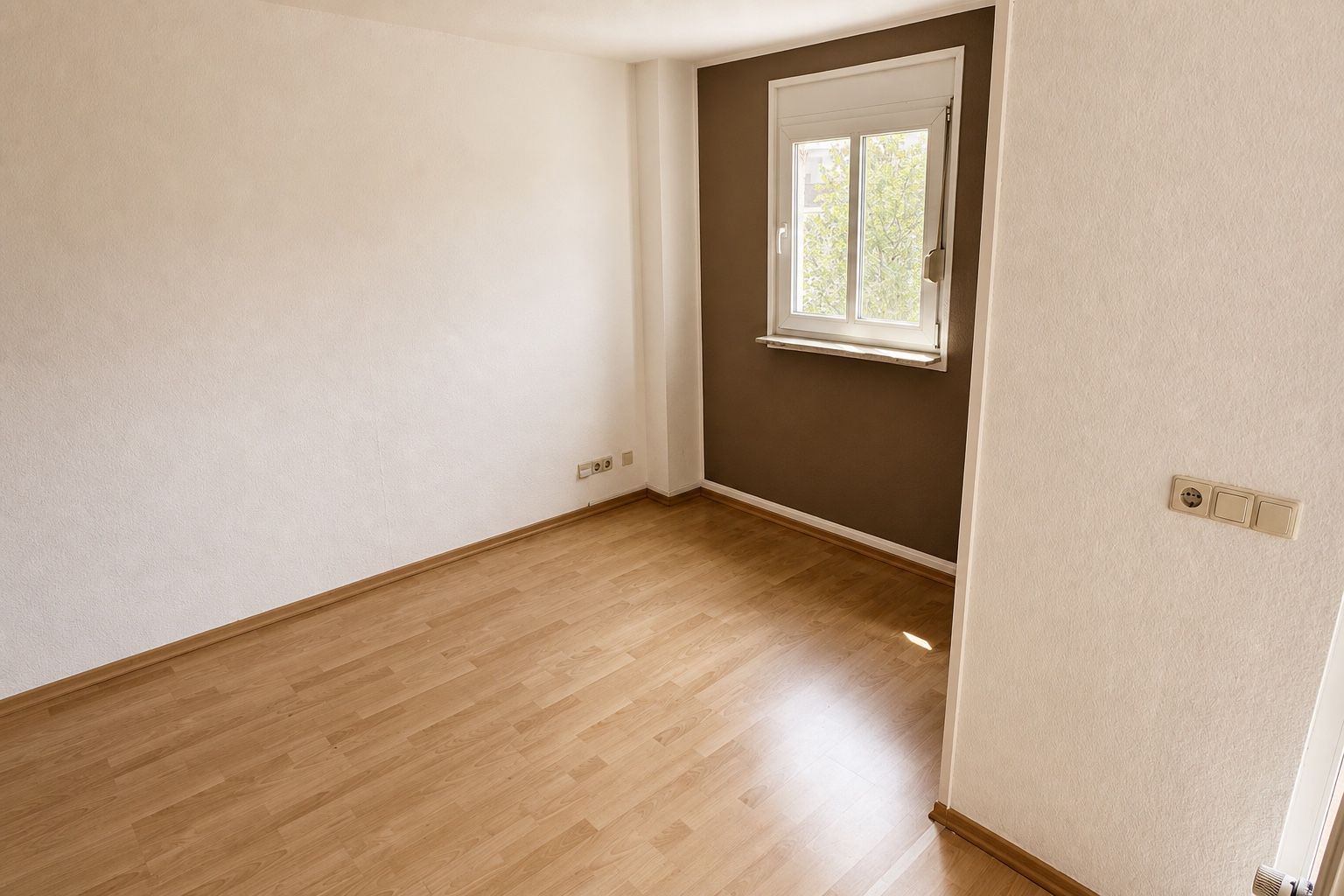 Unmöbliertes Zimmer mit Holzboden, brauner Akzentwand und Fenster zum begrünten Innenhof